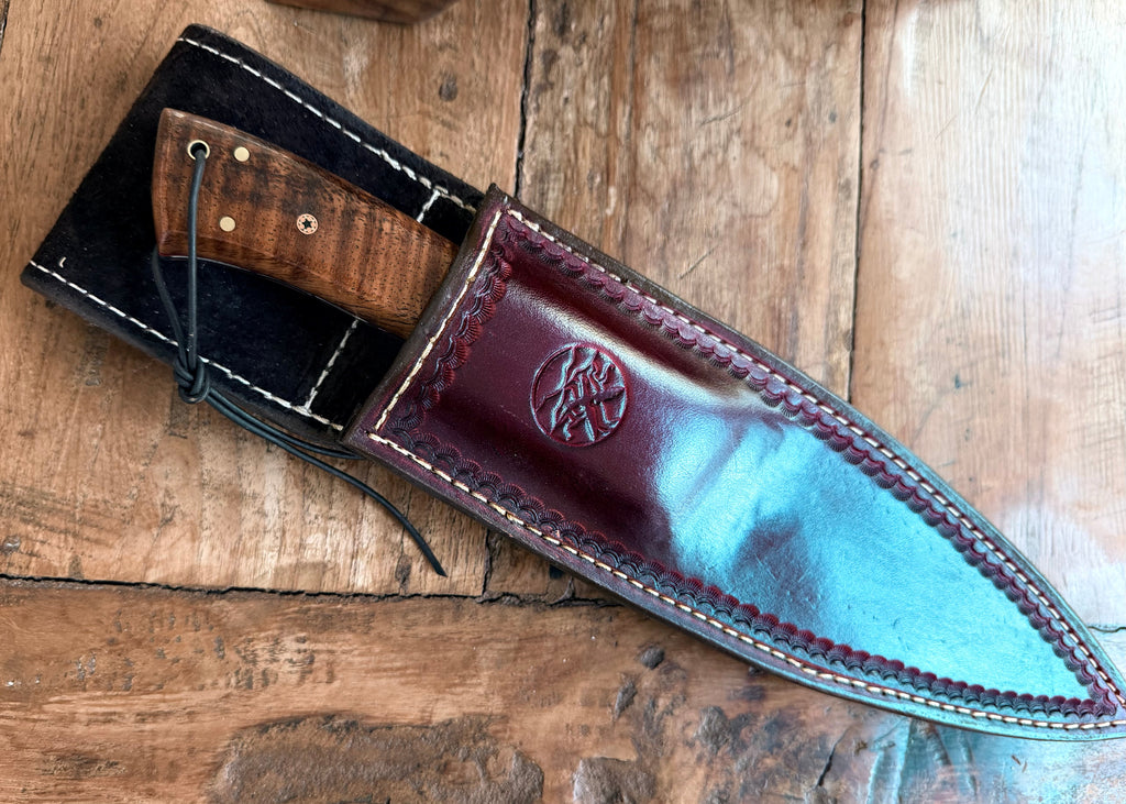 Handcrafted leather sheath containing a custom hand-forged knife with a koa wood decorative handle, The sheath is made of dark reddish-brown leather with white stitching and embossed Salter FineCutlery logo